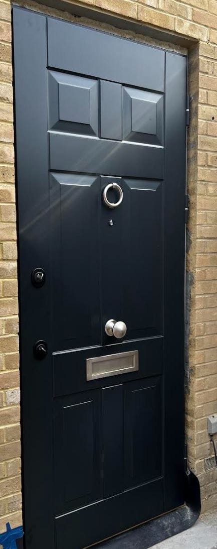 Chrome ring knocker detail on a navy steel entrance door