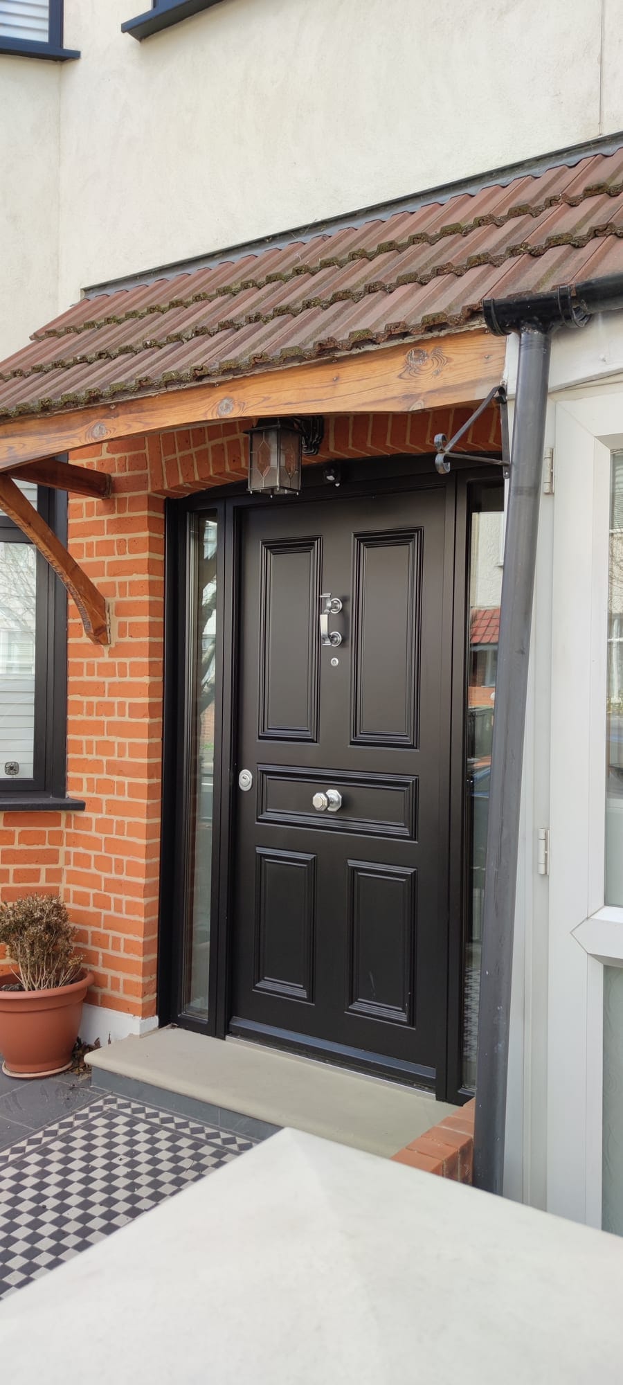 Black traditional 5-panel steel door with doctor knocker under tiled canopy