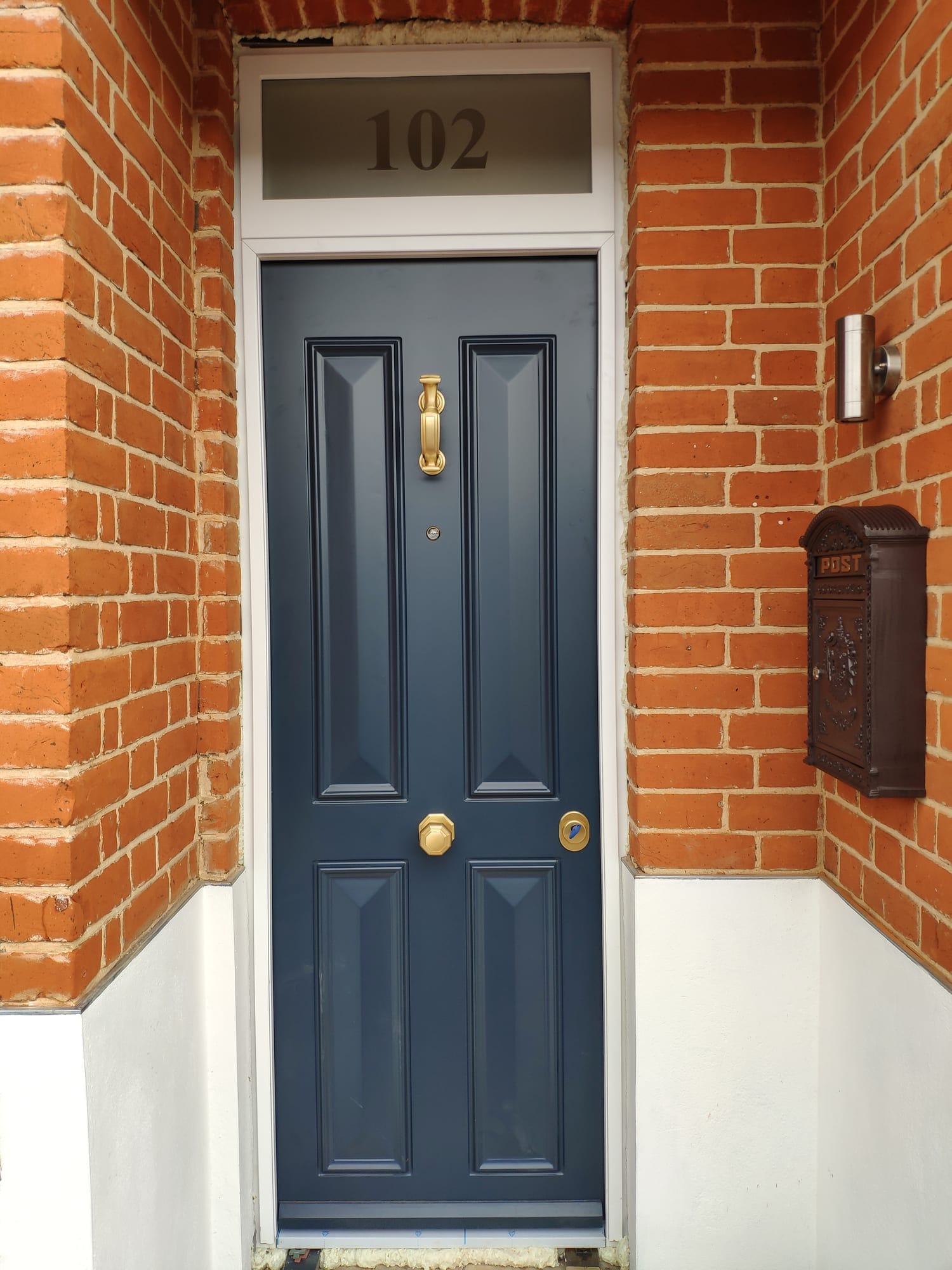 Navy traditional 4-panel steel door with brass hardware and number 102 fanlight