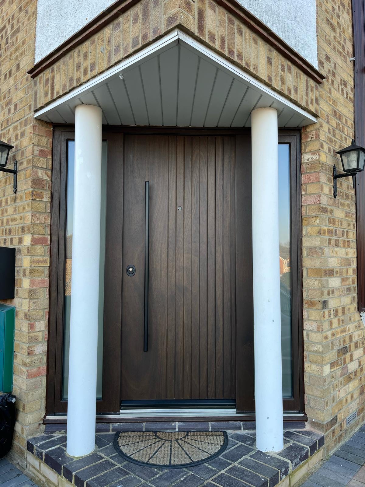 Walnut-finish steel entrance door with ribbed panels between classical columns — front door replacement