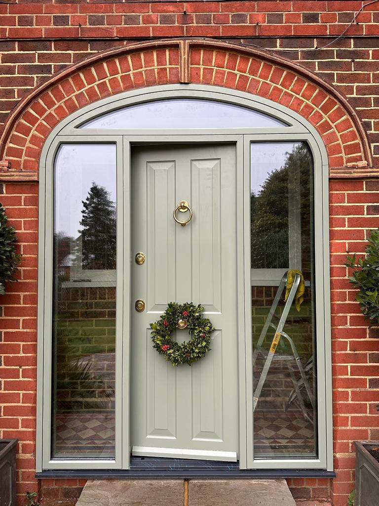 Sage green panelled steel door under arched brick surround